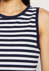 Marinblå och vit randig ärmlös topp med rund halsringning, tillverkad av mjukt tyg; har jämnt fördelade horisontella ränder och en enkel skärning.
