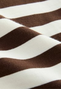 Raitapintaisesta neuloksesta, joka on ruskea ja valkoinen, löytyy vaakasuoria raitoja eri leveysasteissa. Kankaan pinta on pehmeä ja sileä.