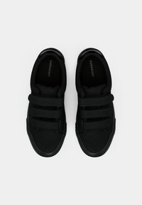 Czarne trampki z teksturowanym materiałowym wierzchem, trzema paskami na rzep oraz gumową podeszwą o zaokrąglonym kształcie przodu. Subtelne oznaczenie marki wewnątrz.