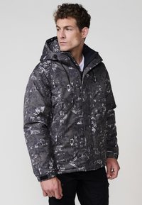 Chaqueta acolchada con estampado en blanco y negro, con capucha, cierre de cremallera, cordones ajustables y un material texturizado.