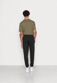 T-shirt verde oliva con vestibilità rilassata, abbinata a pantaloni di felpa neri con polsini elastici. Il modello indossa sneaker bianche.