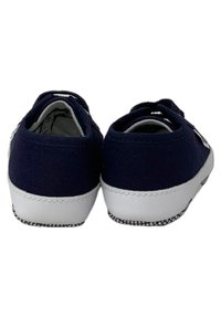 Scarpe di tela blu navy con suole in gomma bianche, caratterizzate da un design semplice e dettagli di cucitura. La vista posteriore mostra lati elastici per una facile calzata.