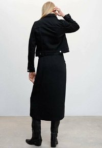 Giacca di jeans nera con un design accorciato, abbinata a una lunga gonna nera e stivali neri fino al ginocchio. Texture liscia e stile minimalista.