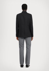 Svart kavaj med skräddarsydd passform, enkel vent, och knappade manschetter, parat med grå raka jeans och svarta skor.