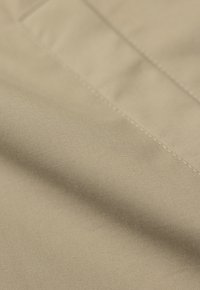 Beżowy materiał o gładkiej teksturze i subtelnym połysku. Posiada ciasny splot z widocznymi ściegami. Miękki, lekki materiał, delikatnie układający się.