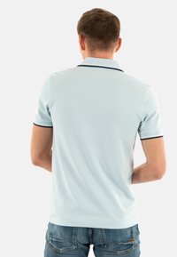 Polo shirt azzurro chiaro con colletto a coste, con dettagli blu navy sul colletto e sulle maniche; tessuto testurizzato. Indossato con jeans di denim.
