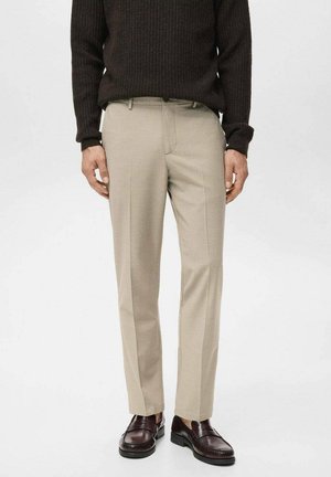 Pantalones beige de corte recto con una textura suave, presentan un frente plano, bolsillos laterales y una pierna ajustada, combinados con un suéter oscuro texturizado y zapatos.