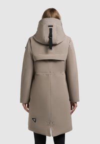 Beige, long parka with a large hood, smooth texture, front snap closure, side pockets, and a black accent tag near the hem.