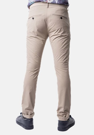 Pantaloni beige slim-fit con due tasche posteriori e chiusure a zip, abbinati a sneakers nere. Tessuto morbido e design su misura.