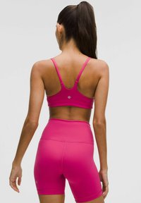 Sutien sport fucsia și pantaloni scurți dintr-un material neted și elastic. Pantalonii scurți au talie înaltă și lungime până la mijlocul coapsei. Brandul este minimal pe spate.