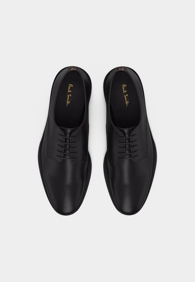 Μαύρα επίσημα δερμάτινα παπούτσια με κορδόνια και στρογγυλεμένες μύτες, με μαρκάτα πέλματα που γράφουν "Paul Smith", τοποθετημένα δίπλα-δίπλα σε λευκό φόντο.