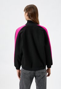 Czarny sweatshirt z różowymi akcentami, wysoki kołnierz i ribbowe mankiety. Charakteryzuje się luźnym krojem i miękkim, teksturowanym materiałem.