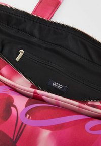 Interno della borsa a mano con stampa floreale rosa, caratterizzato da un rivestimento in tessuto nero e una tasca con zip. Ferramenta della cerniera dorata e un'etichetta del marchio visibile.