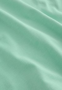 Tissu vert menthe doux avec une texture subtile et des plis délicats créant des courbes lisses et fluides à la surface.