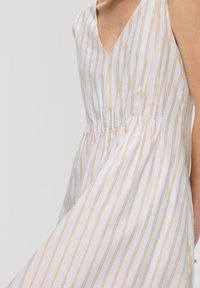 Vestido blanco con rayas doradas verticales, con un diseño de escote en V, cintura fruncida y tela ligera. Textura suave con un brillo sutil.