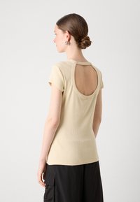 Kortsleeve, ribbet beige topp med scoop-back design og en tettsittende silhuett, kombinert med svarte cargo-bukser med sidelommer.