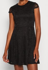 Svart spetsklänning med korta ärmar, rund halsringning, blommönster, figurnära liv och utsvängd kjol, textil med intrikata detaljer.