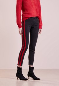 Svarta jeans med röda sidostripes, figurnära design och ankellång klipp, kombinerat med en röd stickad tröja och svarta klackade ankelskor.