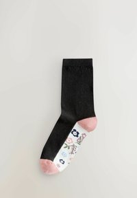Socquette noire à la cheville avec un talon rose, présentant un motif floral en bleu, rose et vert sur un fond blanc. Texture lisse et tricotée.