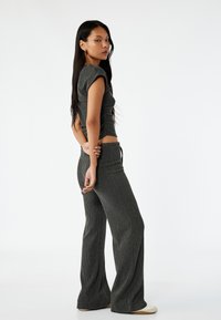 Grijs geribbeld tweedelig set bestaande uit een cropped, aansluitend top met korte mouwen en high-waisted, uitlopende broeken. Gladde textuur en zachte stof.