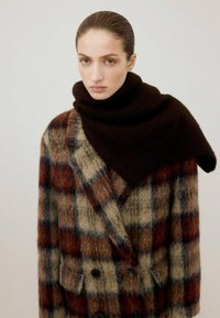 Abrigo cruzado con patrón a cuadros en marrón, beige y azul, combinado con una bufanda marrón oscuro. Textura de mezcla de lana, bolsillos delanteros visibles.