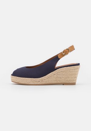Zapato cuña slingback azul marino con correa ajustable marrón, puntera abierta y tacón plataforma de yute trenzado sobre fondo blanco.