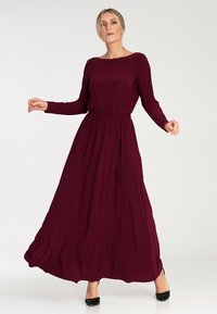 Burgundowa maxi sukienka z długim rękawem, okrągłym dekoltem, elastycznym pasem i zwiewnym dołem, wykonana z lekkiego, gładkiego materiału.