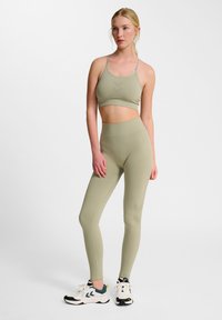 Ljust grön sport-bh med tunna remmar, tillsammans med högmidjade leggings. Texturerat mönster på leggingsen. Vita träningsskor med blå accenter.