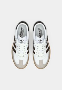 White athletic shoes featuring brown stripes, suede accents, and a textured rubber sole. Lace-up style with a padded collar and tongue.