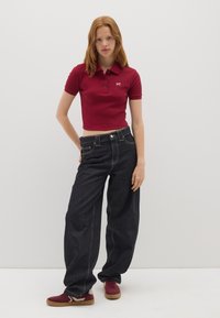 Rotes, kurzes Polohemd mit kurzen Ärmeln und drei Knöpfen. Dunkelblaue, weite Jeans mit vorderen Taschen. Burgunderfarbene Sneakers mit cremefarbenen Akzenten.