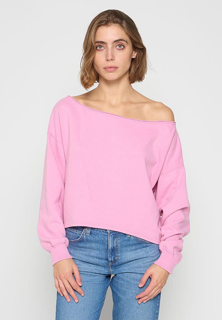 Rosa gecroppter Sweatshirt mit schulterfreiem Ausschnitt, langen Ärmeln und weichem Material. Kombiniert mit blauen Jeans.