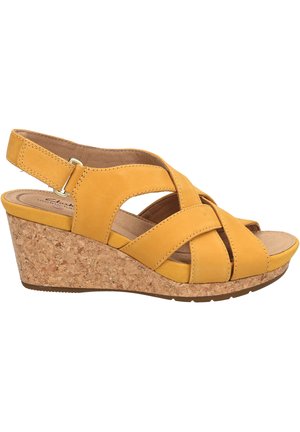 Sandalia cuña amarilla con tiras cruzadas, tacón de corcho y correas traseras ajustables. Material superior suave y plantilla acolchada.