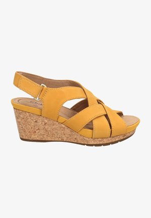 Sandalia cuña amarilla con tiras cruzadas, tacón de corcho y correas traseras ajustables. Material superior suave y plantilla acolchada.