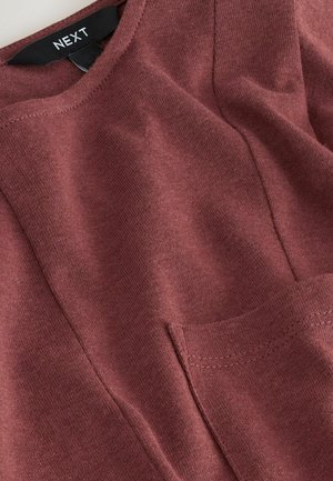 Bordeauxrotes Baumwolloberteil mit rundem Ausschnitt, einer Brusttasche, strukturierter Stoff und sichtbaren Nahtdetails.