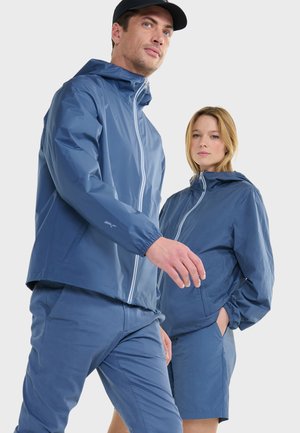 Des vestes imperméables bleues avec des capuches et des poignets élastiques, accompagnées de pantalons et de shorts bleus assortis, comportent des zips légers et une texture lisse.