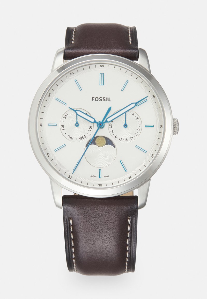 Montre en acier inoxydable argenté avec un cadran blanc, des aiguilles bleues et un bracelet en cuir marron. Présente des indicateurs de date et de jour, ainsi qu'un détail sur la phase de la lune.