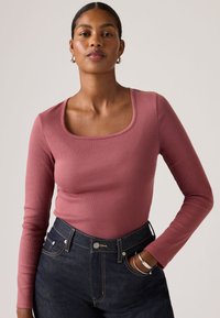 Μπλούζα με μακριά μανίκια και ριμπ ύφανση σε χρώμα σκόπιου ρόζ με τετράγωνο λαιμόκοψη. Συνδυάζεται με ψηλόμεσα σκούρα τζιν και ασημένιο βραχιόλι στον καρπό.