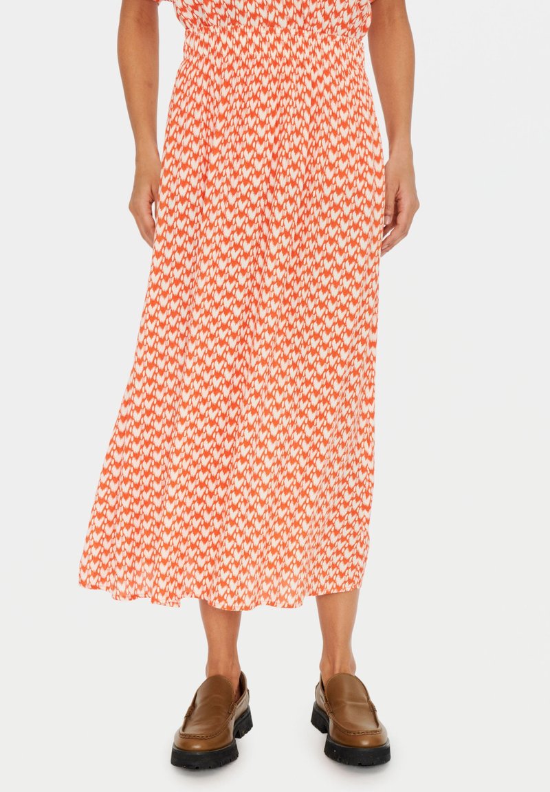 Jupe midi avec motif géométrique orange et blanc, portée avec des mocassins marron épaisses, montrant le bas du corps de la taille jusqu'aux pieds.