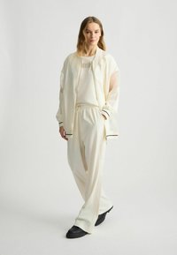 Crème-kleurige sportoutfit bestaande uit een lichte zip-up bomberjack met mesh-mouwen en een relaxed-fit broek met een elastische tailleband.