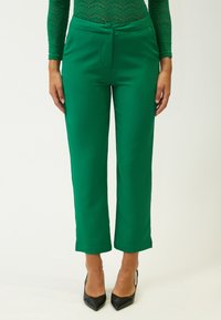 Groene, op maat gemaakte wijde broek met een gladde textuur, voorzien van een vlakke sluiting aan de voorkant en een schone zoom, gecombineerd met pointed zwarte hakken.