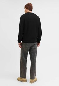 Suéter negro de punto con mangas largas, combinado con jeans gris desgastado y calzado beige. El modelo lleva un gorro marrón.