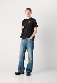 Black cotton T-shirt with white logo, paired with light blue ripped jeans. Black shoes and a small black shoulder bag.