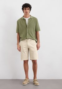 Green short-sleeve button-up shirt, beige shorts, and beige shoes. Soft texture, relaxed fit, casual design. No notable patterns or accents.