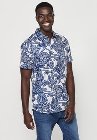 Camicia a maniche corte con bottoni, in motivo floreale blu e bianco, realizzata in tessuto leggero, con colletto e piccoli bottoni marroni.