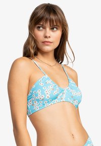 Blå blomstret bikinioverdel med tynne stropper, med en samlet midtdel og små hvite og gule blomstermønstre på et glatt stoff.