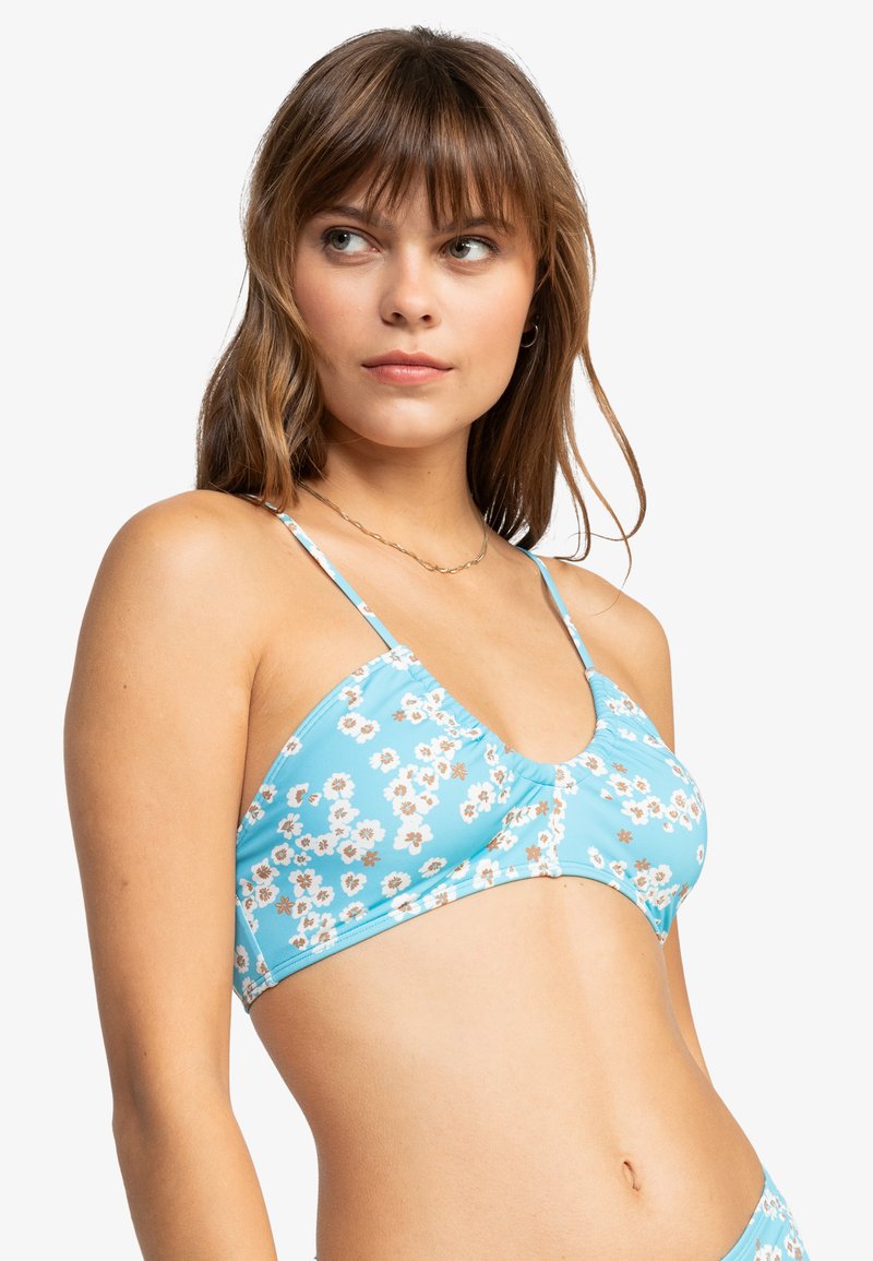 Blå blomstret bikinioverdel med tynne stropper, med en samlet midtdel og små hvite og gule blomstermønstre på et glatt stoff.