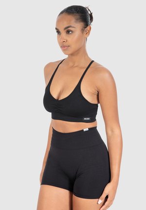 Zwarte sportbeha met verstelbare banden en geplooid voorpand, gecombineerd met zwarte high-waisted shorts, beide in een gladde stof.