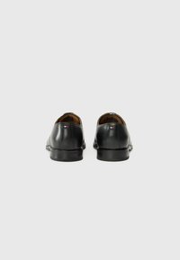 Zapatos de vestir de cuero negro con una textura suave, punta redondeada, tacón bajo y costuras sutiles. El interior presenta forro marrón y marca.