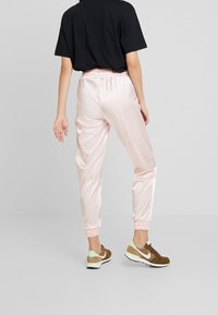 Satinrosa joggers med elastisk midja och muddar, i kombination med bruna sneakers med gröna detaljer och en svart T-shirt.