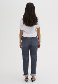 Jeans in denim blu scuro con orlo arrotolato e taglio classico, dotati di tasche posteriori e una leggera scoloritura, abbinati a una t-shirt bianca semplice.